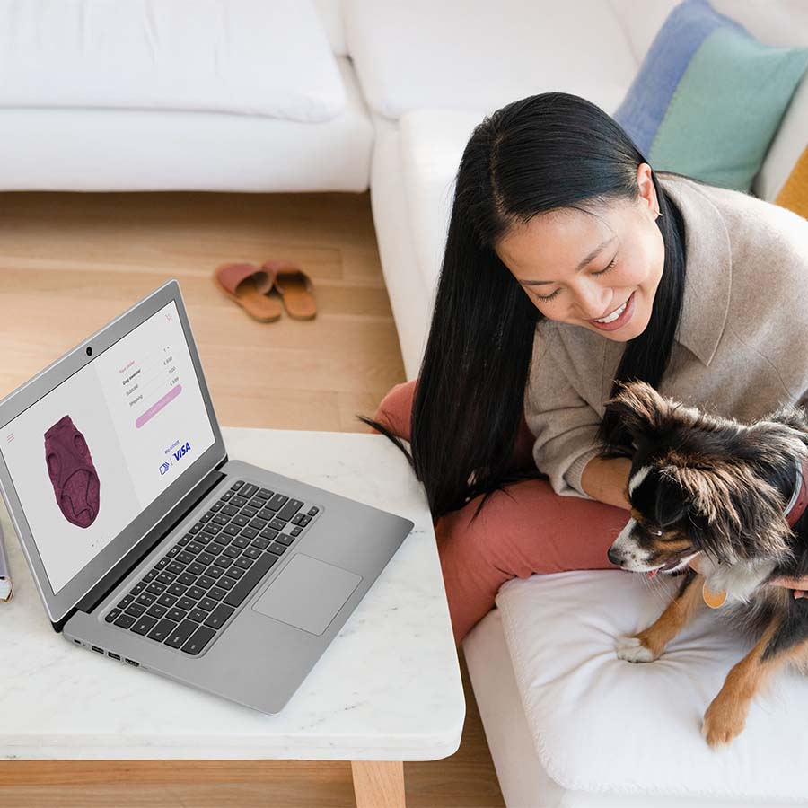 woman smiling at dog on sofa with laptop displaying Visa Checkout