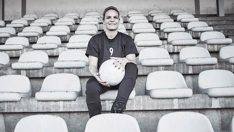 Eugenie Le Sommer sitting in football stadium and holding a football in her lap.